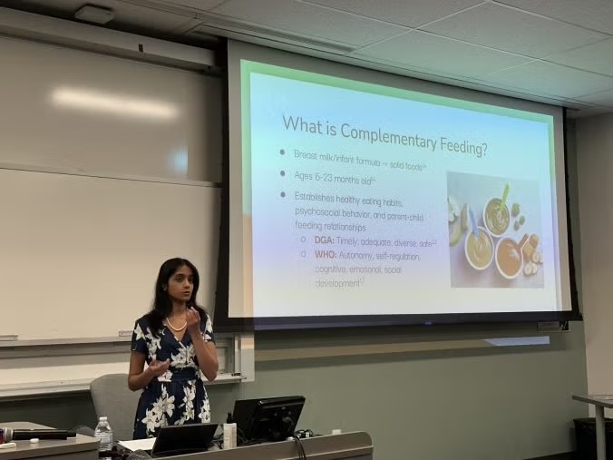 Woman presenting in classroom, slide with fruit illustration about complementary feeding